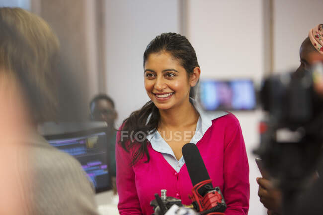 Sonriente, confiada estudiante de periodismo universitario comunitario detrás del micrófono - foto de stock