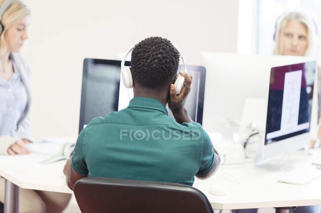 Estudiante universitario de comunidad masculina con auriculares usando computadora en laboratorio de computación - foto de stock