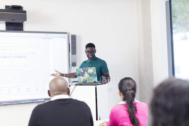 Male community college instructor teaching lesson at laptop and projection screen in classroom — Stock Photo