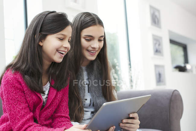 Счастливые сестры с помощью цифрового планшета на диване гостиной — стоковое фото