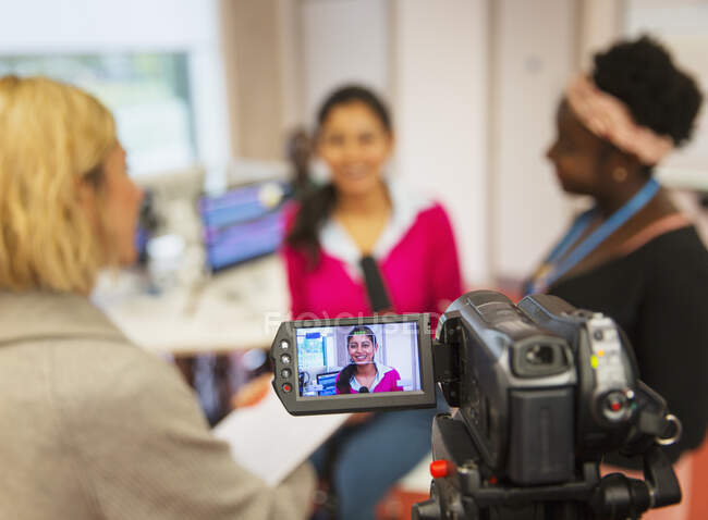 Videocámara filmando estudiantes de periodismo universitario comunitario femenino en el aula - foto de stock