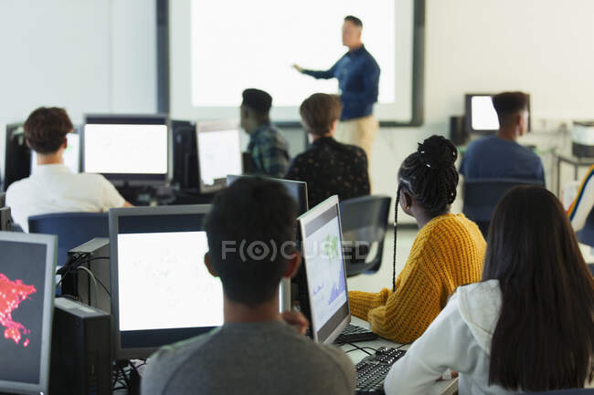 Étudiants du secondaire aux ordinateurs regardant l'enseignant à l'écran de projection en classe — Photo de stock