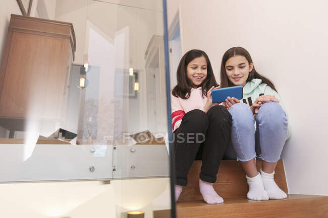 Schwestern nutzen Smartphone auf der Treppe zu Hause — Stockfoto