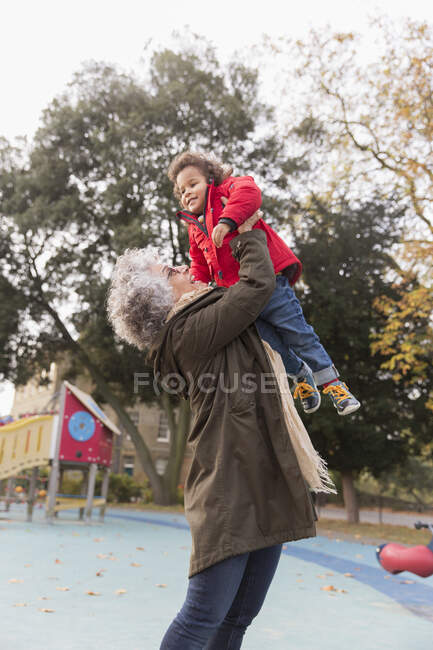 Grand-mère levant petite-fille à l'aire de jeux — Photo de stock