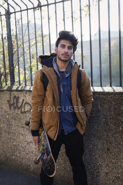 Portrait confiant jeune homme tenant skateboard — Photo de stock