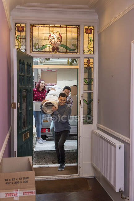 Друзі рухають будинок, переносячи килим через вхідні двері — стокове фото