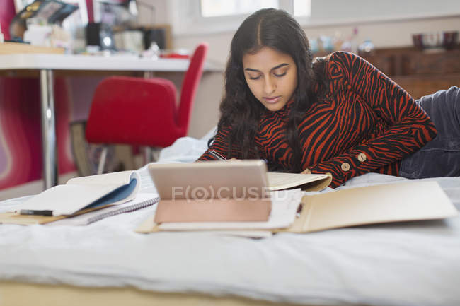 Орієнтована дівчина-підліток робить домашнє завдання на ліжку — стокове фото