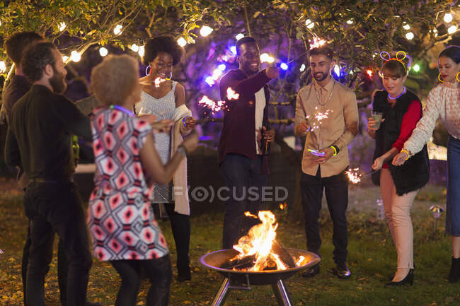 Friends with sparklers around fire pit at garden party — Stock Photo