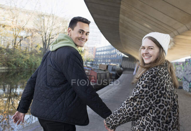 Retrato feliz joven pareja cogida de la mano, caminando a lo largo del canal - foto de stock