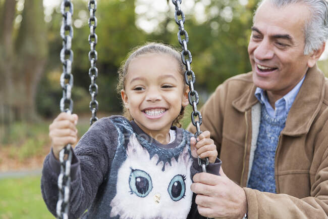 Игривый дедушка и внучка на качелях на детской площадке — стоковое фото