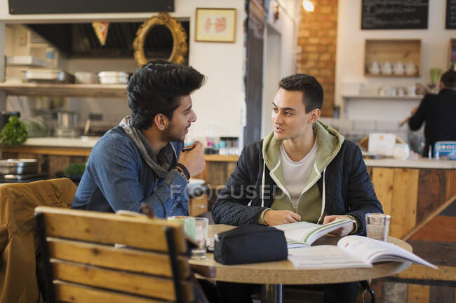 Молодые студенты колледжей учатся и разговаривают в кафе — стоковое фото