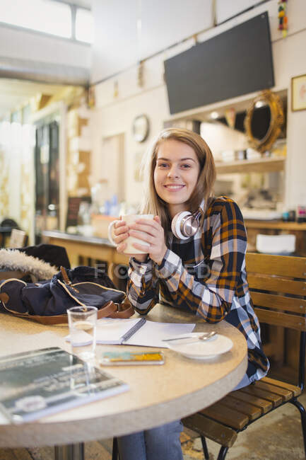 Retrato confiado joven estudiante universitaria bebiendo café y estudiando en la cafetería - foto de stock