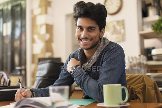 Retrato confiado joven estudiante universitario masculino que estudia en la mesa de café - foto de stock