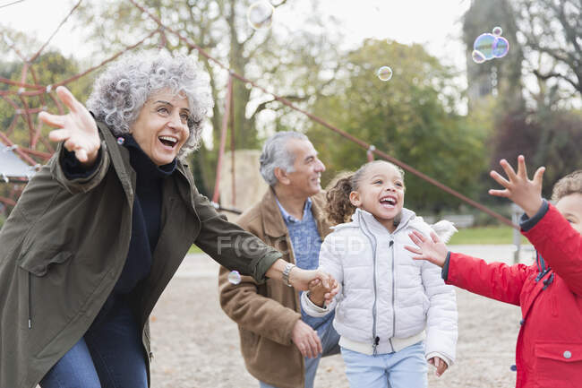 Играющие бабушки и дедушки и внуки играют с пузырьками в парке — стоковое фото