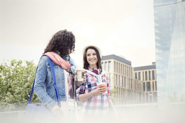 Jóvenes amigas con café caminando por la ciudad - foto de stock