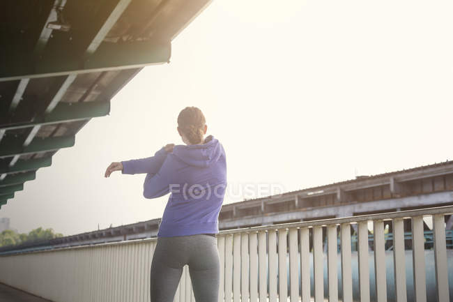 Молодая бегунья протягивает руки вдоль городских перил — стоковое фото