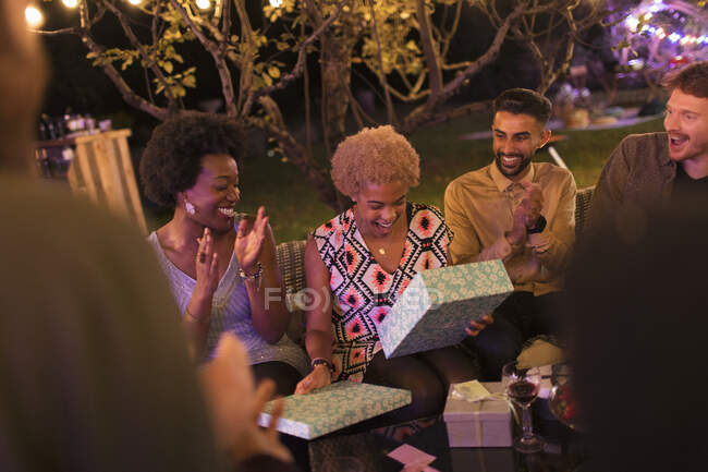 Друзі дивляться, як жінка відкриває подарунок на день народження на садовій вечірці — стокове фото