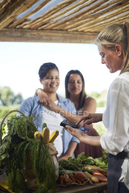 Pareja lesbiana pagando con tarjeta de crédito en el mercado de agricultores - foto de stock