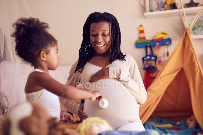 Linda hija pequeña con taza de té tocando el vientre de las madres embarazadas - foto de stock