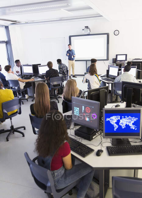 Junior high students at computers listening to teacher at projection screen in classroom — Stock Photo
