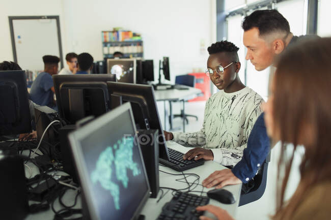 Homme premier cycle du secondaire enseignant aider garçon étudiant en utilisant l'ordinateur dans le laboratoire informatique — Photo de stock
