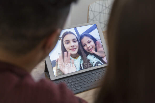 Дочери на цифровом планшете машут родителям, видеоконференции с родителями — стоковое фото
