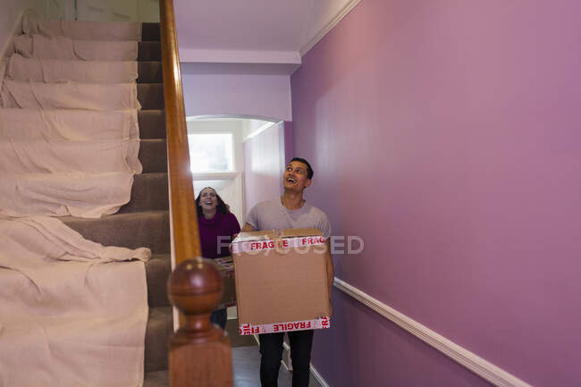 Pareja feliz mudándose a casa nueva, llevando cajas de cartón en el pasillo - foto de stock