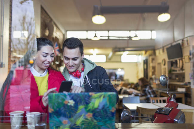 Молодая пара, использующая смартфон у окна кафе — стоковое фото