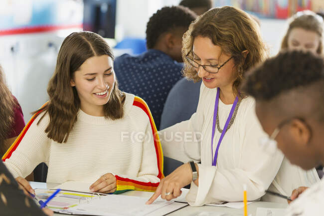 Female high school teacher helping girl student with homework in classroom — Stock Photo