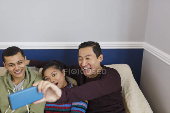 Amigos felices tomando selfie con teléfono inteligente en el sofá - foto de stock