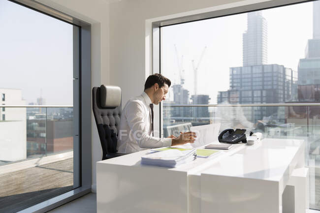 Geschäftsmann überprüft Papierkram in sonnigem, modernem, urbanem Büro — Stockfoto
