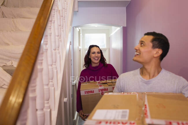 Joyeux couple emménageant dans une nouvelle maison, portant des boîtes en carton dans le couloir — Photo de stock