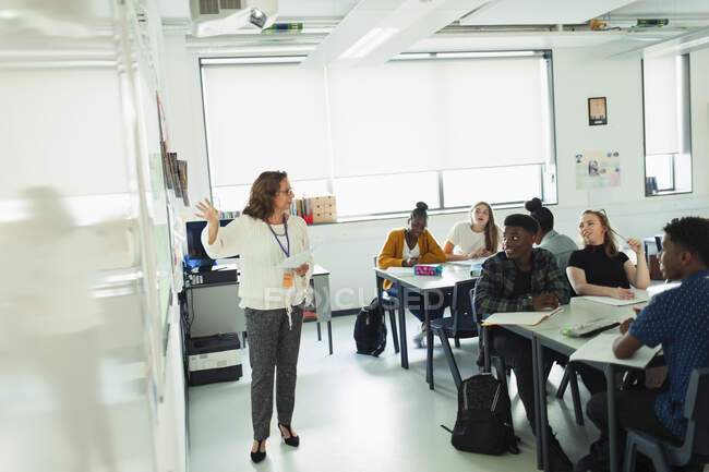 High school students watching teacher leading lesson at whiteboard in classroom — Stock Photo