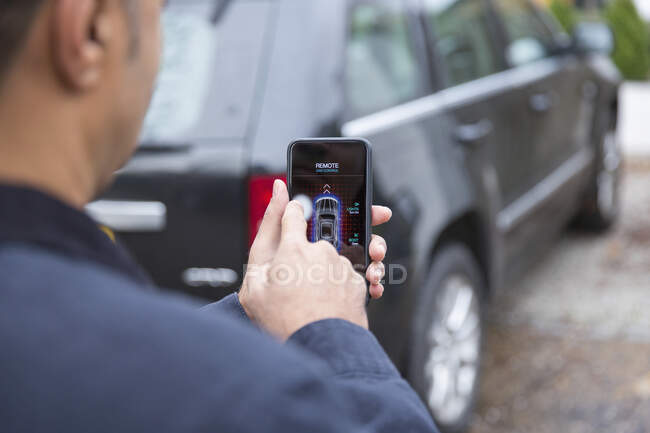 Homem definindo alarme carro com telefone inteligente na entrada de carro — Fotografia de Stock