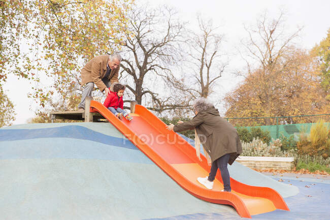 Grandparents playing with grandson on playground slide — Stock Photo