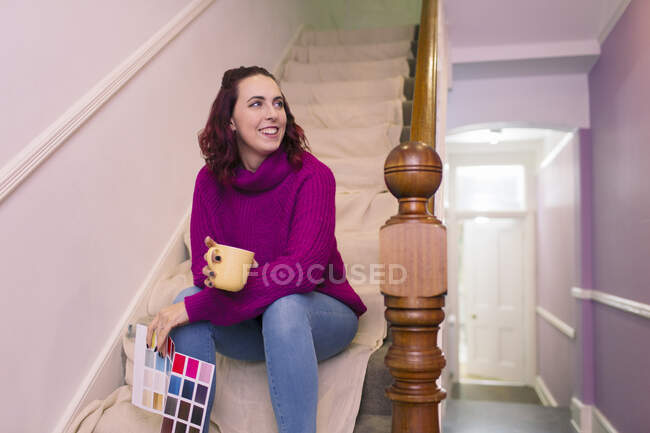 Smiling woman with paint swatches and coffee redecorating on stairs — Stock Photo