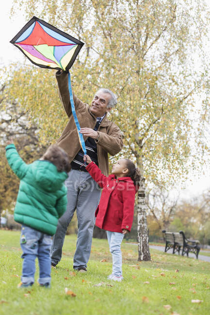Nonno e nipoti che volano con un aquilone nel parco autunnale — Foto stock