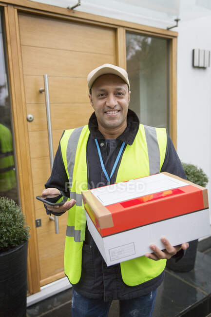 Portrait confident, friendly male deliveryman with smart phone at front door — Stock Photo