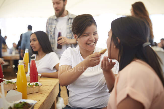 Smiling woman feeding girlfriend food at farmers market — Stock Photo