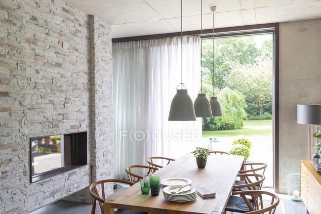 Luzes pingente sobre mesa de jantar na moderna sala de jantar com lareira de tijolo — Fotografia de Stock