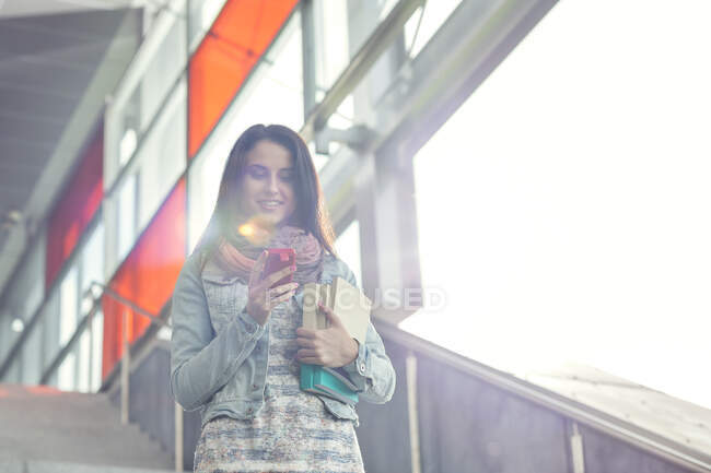 Молода жінка з книгами і смартфон спускається сходами — стокове фото