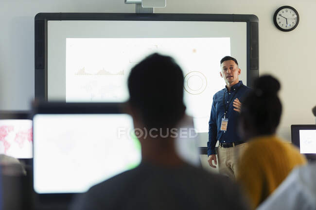 Profesor de secundaria masculino dirigiendo la lección en la pantalla de proyección en el aula - foto de stock