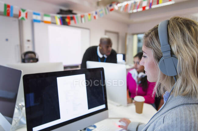 Estudiante universitaria comunitaria con auriculares usando computadora en aula de laboratorio de computación - foto de stock