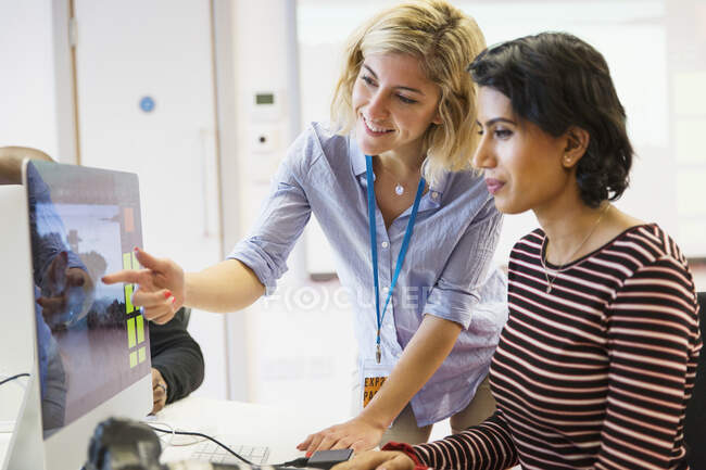 Instrutora de fotografia feminina ajudando estudante em computador em sala de aula — Fotografia de Stock