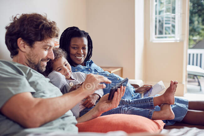 Беременная молодая семья с использованием смартфона и цифрового планшета на диване — стоковое фото