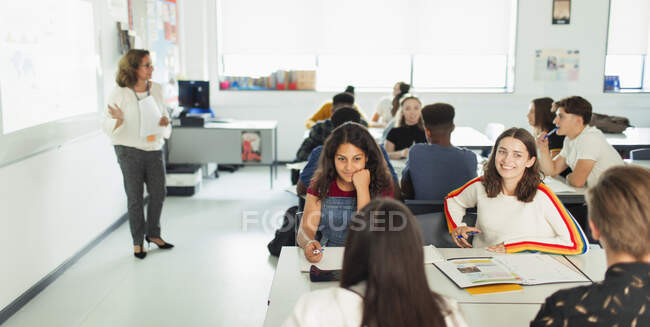 Estudiantes de secundaria hablando en la mesa en el aula durante la lección - foto de stock