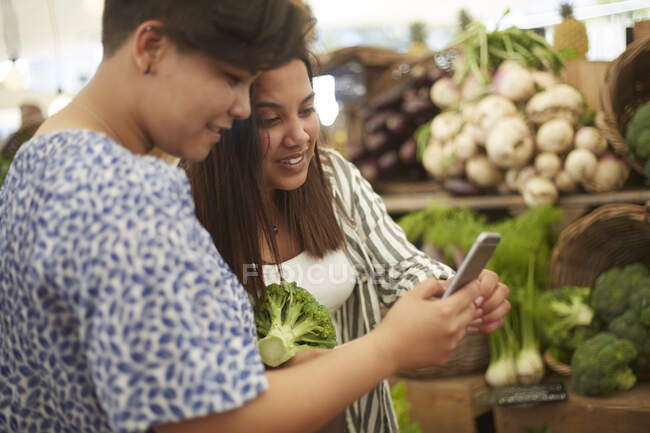 Lésbicas casal com telefone inteligente compras no mercado de agricultores — Fotografia de Stock