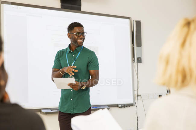 Instrutor da faculdade da comunidade masculina que conduz a lição na tela da projeção na sala de aula — Fotografia de Stock