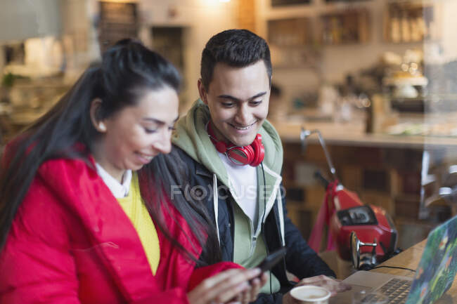 Молодая пара с помощью смартфона и ноутбука в кафе — стоковое фото