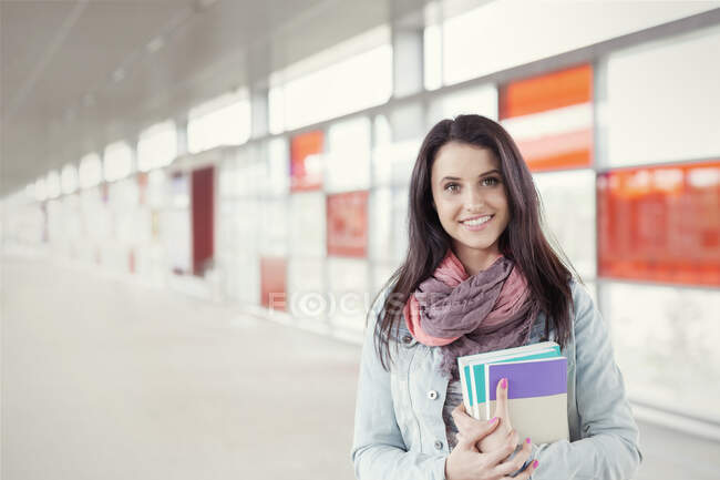 Portrait confident young woman with books standing in urban corridor — Stock Photo